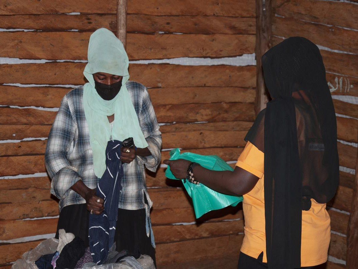 Two women sorting clothing during a distribution inside a timber shelter