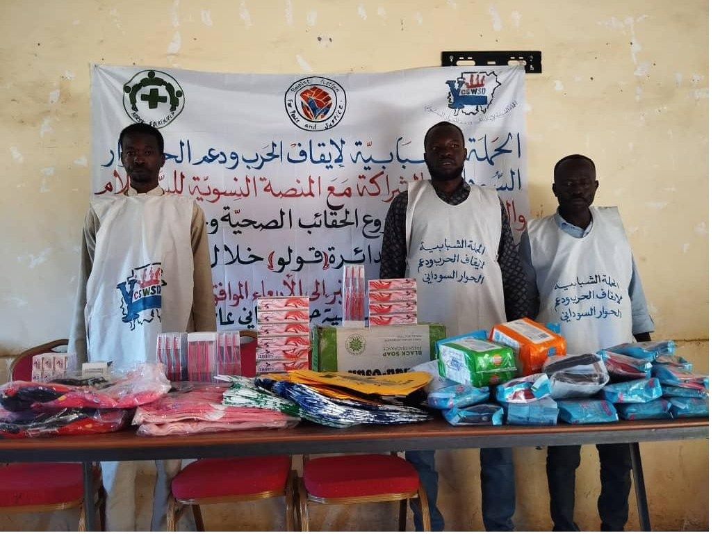 Volunteers standing behind a table of hygiene and clothing supplies prepared for distribution